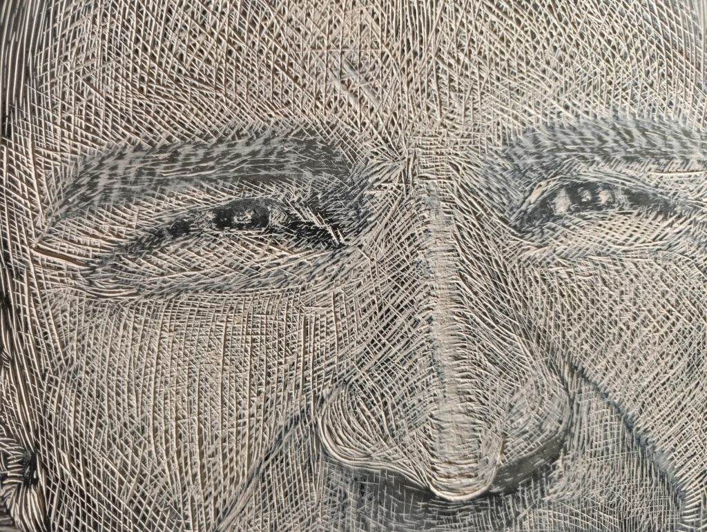 Zbliżenie na fragment matrycy linorytniczej przedstawiającej oczy i nos portretowanej osoby. Widoczna gęsta, krzyżująca się faktura nacięć dłutem, budująca światłocień i rysy twarzy.
