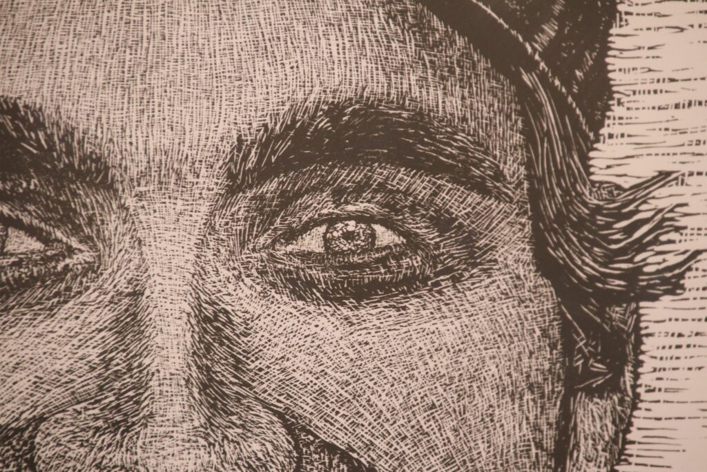 Zbliżenie na fragment linorytu przedstawiający oko i brwi portretowanej osoby. Widoczna gęsta sieć krótkich, krzyżujących się nacięć dłutem, tworzących światłocień i strukturę twarzy.