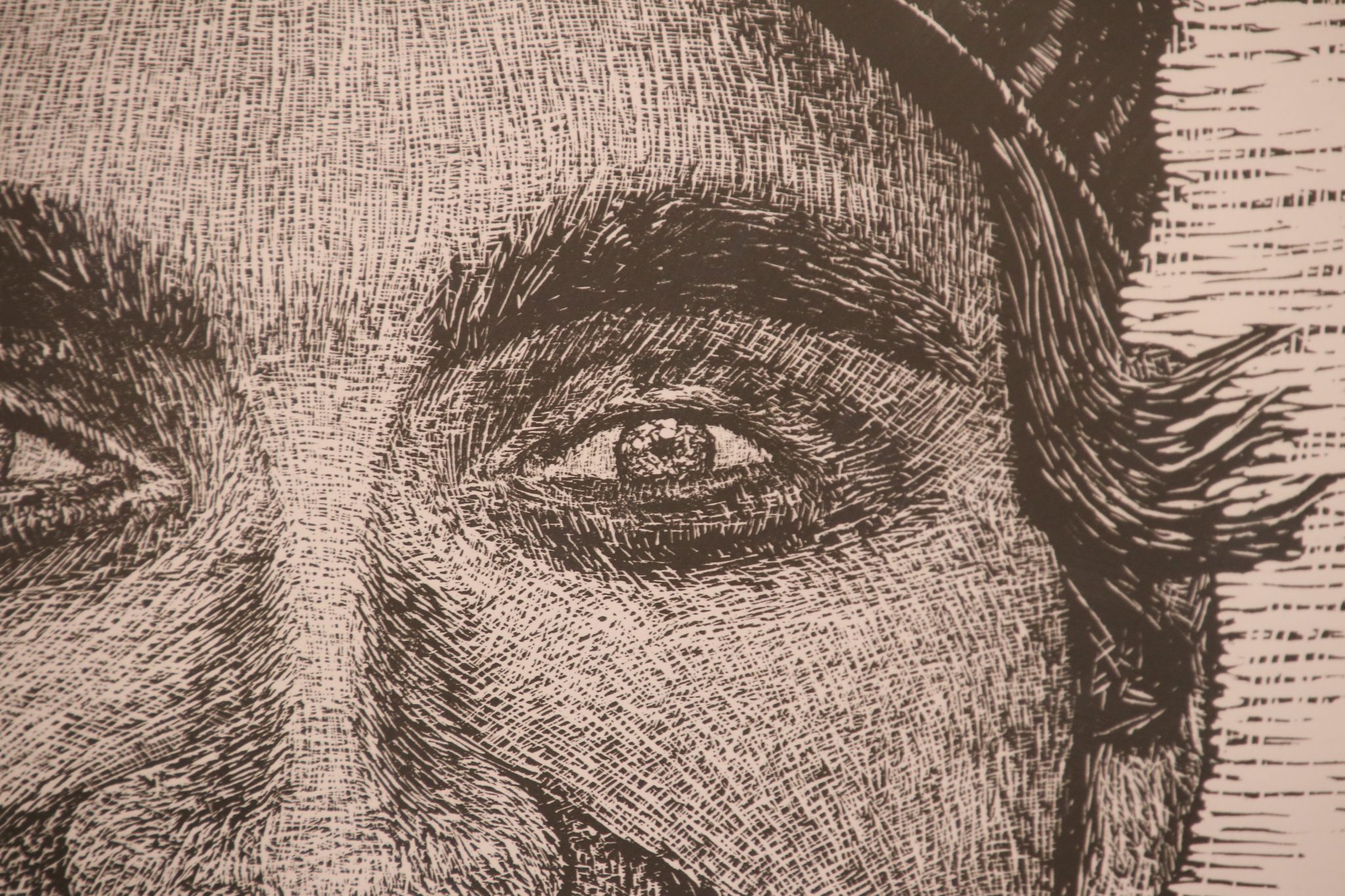 Zbliżenie na fragment linorytu przedstawiający oko i brwi portretowanej osoby. Widoczna gęsta sieć krótkich, krzyżujących się nacięć dłutem, tworzących światłocień i strukturę twarzy.