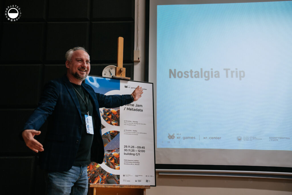Prowadzący Game Jam 2025 stoi na tle czarnych paneli akustycznych, gestykulując z szeroko rozłożonymi ramionami w stronę ekranu z tytułem „Nostalgia Trip”. Obok niego znajduje się duży plakat wydarzenia 8th Game Jam / Metadata ustawiony na sztaludze.