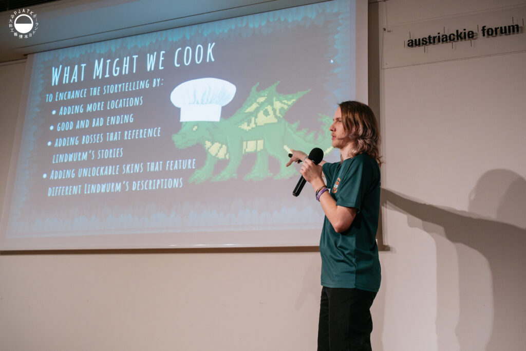 Prelegent wskazuje na slajd z pikselowym smokiem w czapce kucharza i listą pomysłów na rozwój gry.