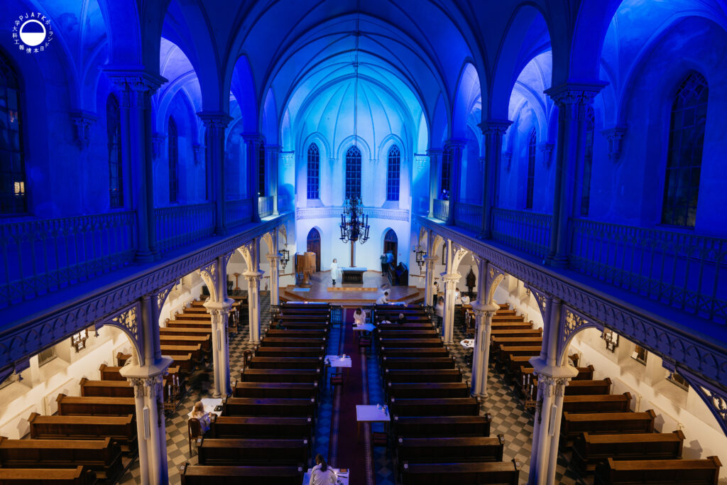 Wnętrze kościoła podświetlone na niebiesko. Kaligrafowie pracują przy stanowiskach rozstawionych po całej świątyni.