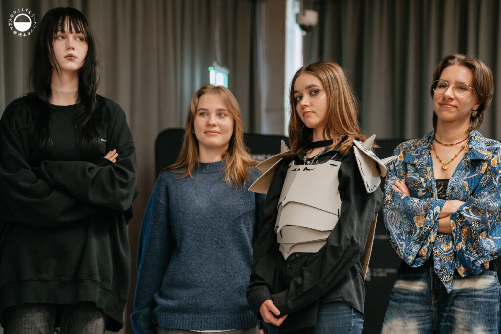 Uczestnicy warsztatów Creativity stoją obok siebie, prezentując prototypy i fragmenty zbroi wykonane w trakcie zajęć.