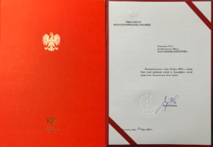 Otwarta czerwona teczka z godłem RP. Po prawej stronie oficjalny dokument Prezydenta Rzeczypospolitej Polskiej nadający tytuł profesora sztuki Pani dr hab. Joannie Marii Walendzik-Stefańskiej, podpisany przez Andrzeja Dudę.