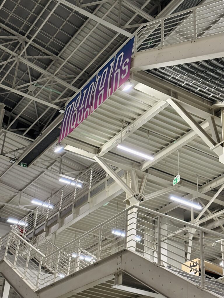 Dokumentacja wystawy „Maintain Mountains – Design for Post-Event Mountain Resilience” na Politecnico di Milano: plansze projektowe „The Vertical Atlas”, model topograficzny z warstwowymi poziomicami oraz przestrzeń ekspozycyjna z dużymi banerami i instalacją w industrialnym wnętrzu kampusu.