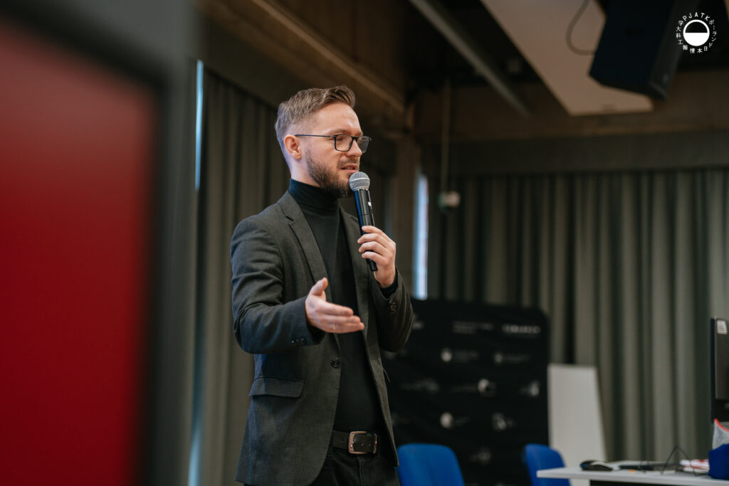 Mężczyzna w garniturze mówi do mikrofonu podczas prezentacji w auli.