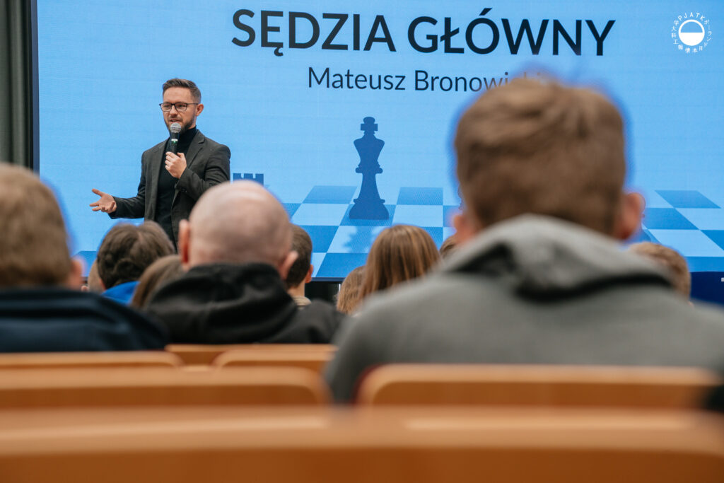 Mężczyzna w garniturze mówi do mikrofonu podczas prezentacji w auli.