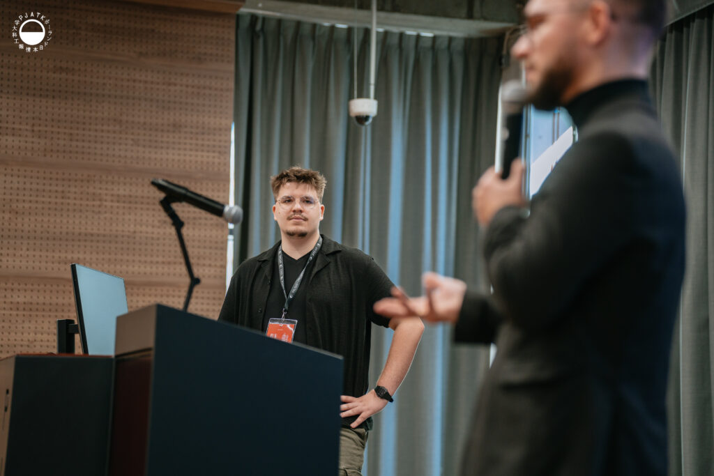 Mężczyzna w garniturze mówi do mikrofonu podczas prezentacji w auli.