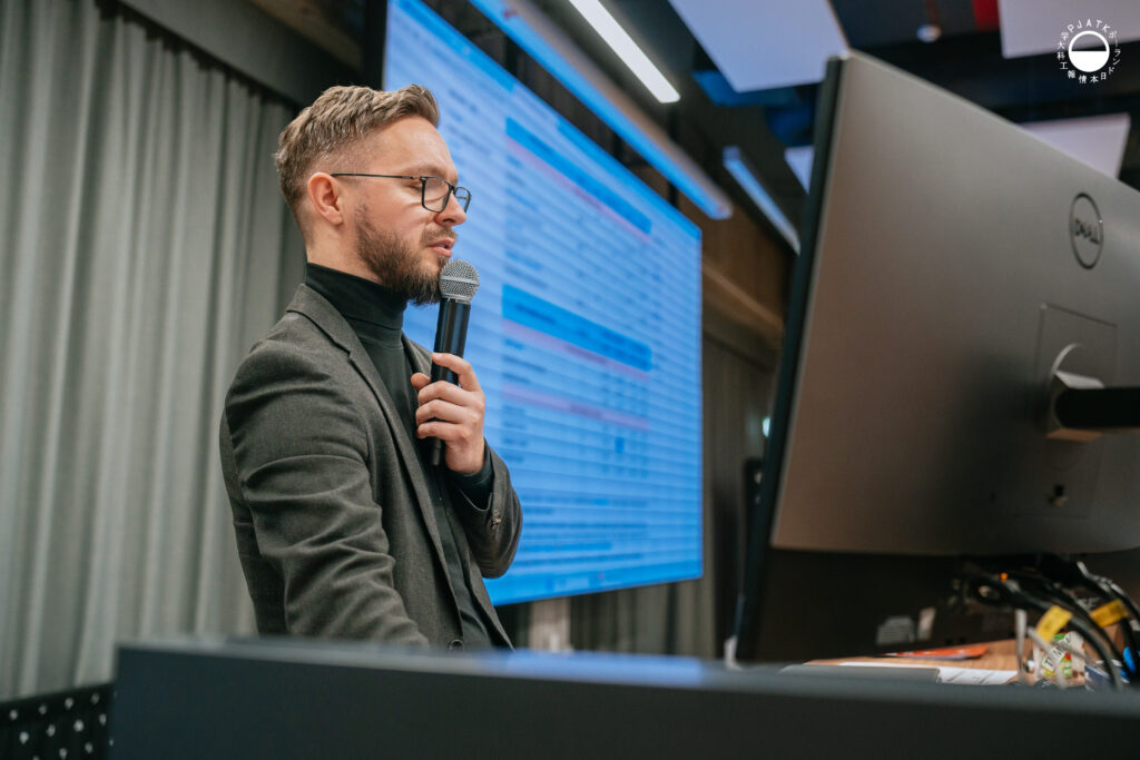 Mężczyzna w garniturze mówi do mikrofonu podczas prezentacji w auli.