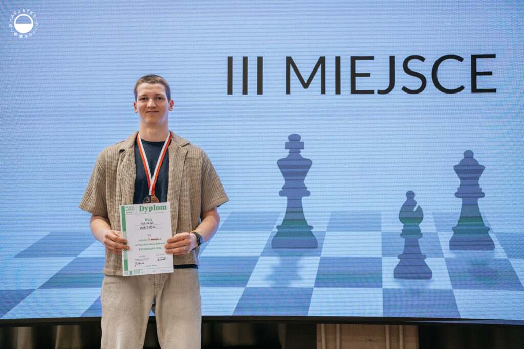 Zwycięzcy turnieju szachowego stoją na scenie z medalami i dyplomami.