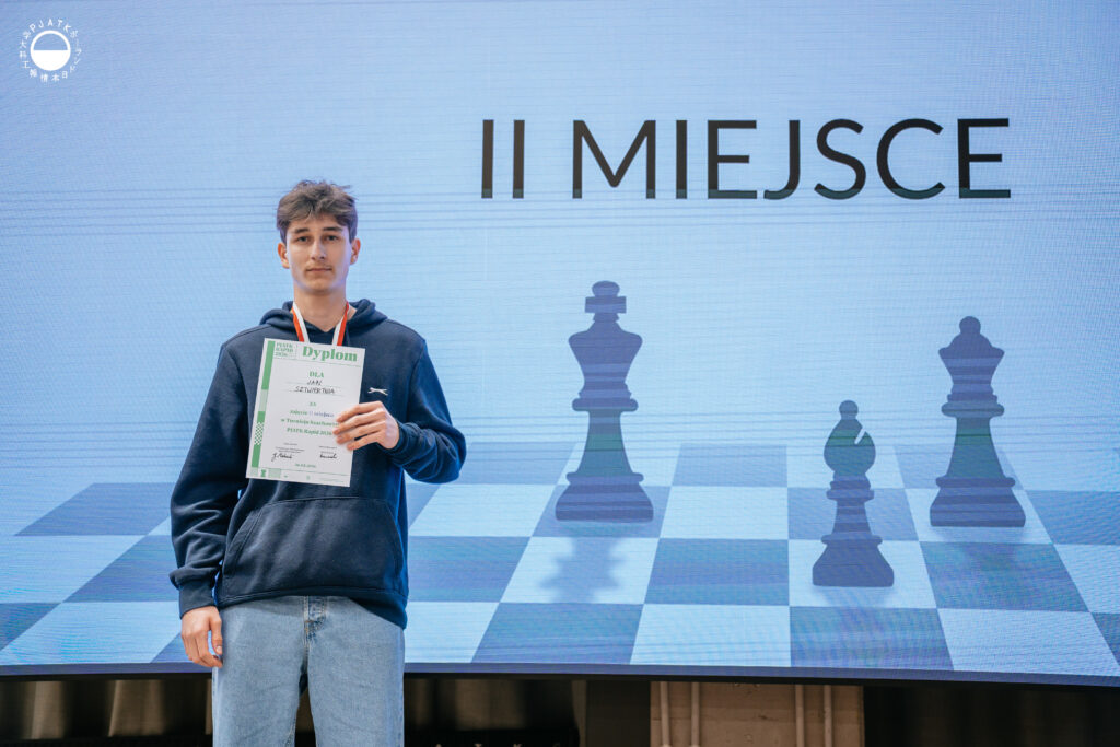 Zwycięzcy turnieju szachowego stoją na scenie z medalami i dyplomami.