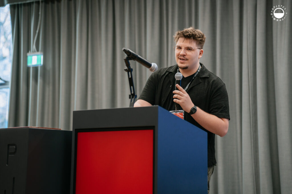 Prelegent przemawia na scenie podczas wydarzenia w auli PJATK