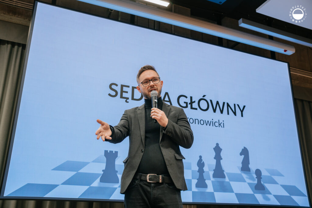 Mężczyzna w garniturze mówi do mikrofonu podczas prezentacji w auli.