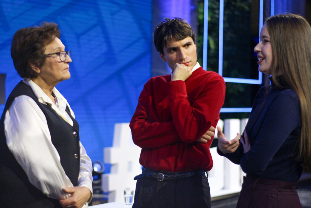 (trzy osoby w rozmowie) Uczestnicy debaty rozmawiają w studiu – młoda kobieta wypowiada się, a pozostali słuchają z uwagą.