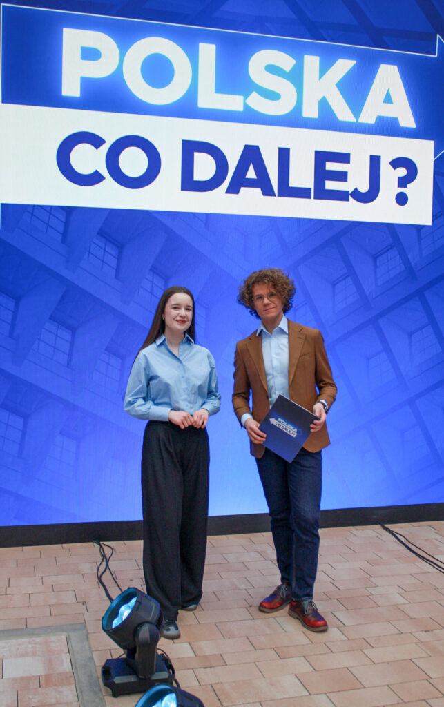 (prowadzący stoją) Prowadzący program „Polska. Co dalej?” stoją w studiu, trzymając materiały do debaty.