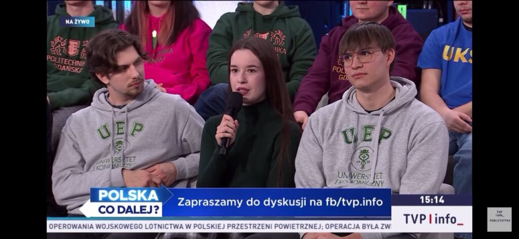 (studio, uczestnicy siedzący, mikrofon) Studentka zabiera głos podczas debaty „Polska. Co dalej?” w studiu telewizyjnym, siedząc wśród innych uczestników.