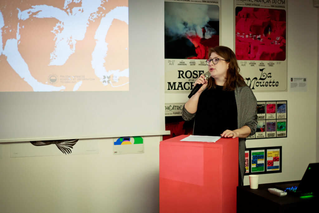 Kobieta przemawia do publiczności podczas wydarzenia, stojąc przy mównicy i ekranie prezentacyjnym.