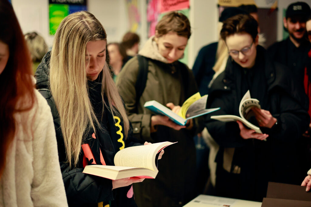 Uczestnicy skupieni na czytaniu książek i publikacji prezentowanych na wystawie.