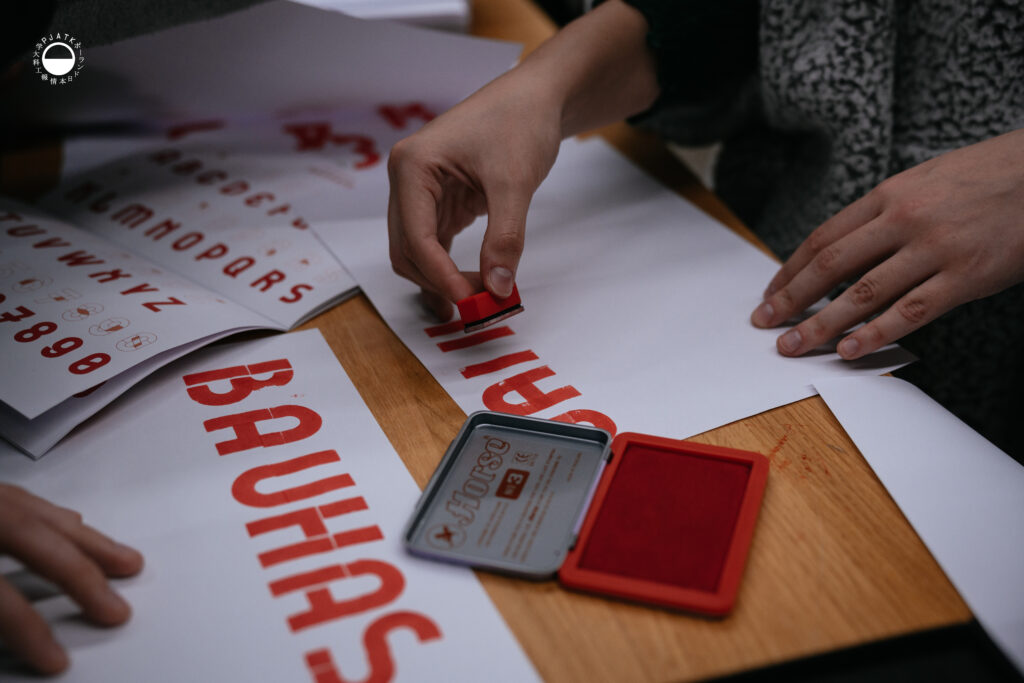 Zbliżenie na ręce odbijające czerwony napis „BAUHAUS” przy użyciu pieczątki.