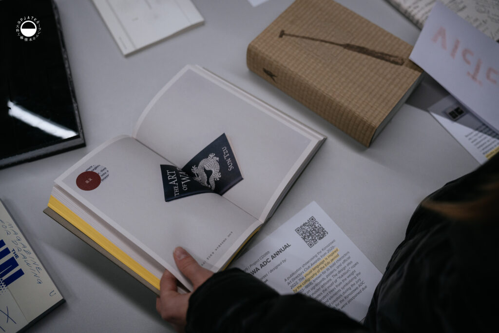 Osoba przegląda książkę typograficzną obok kart informacyjnych z kodami QR.