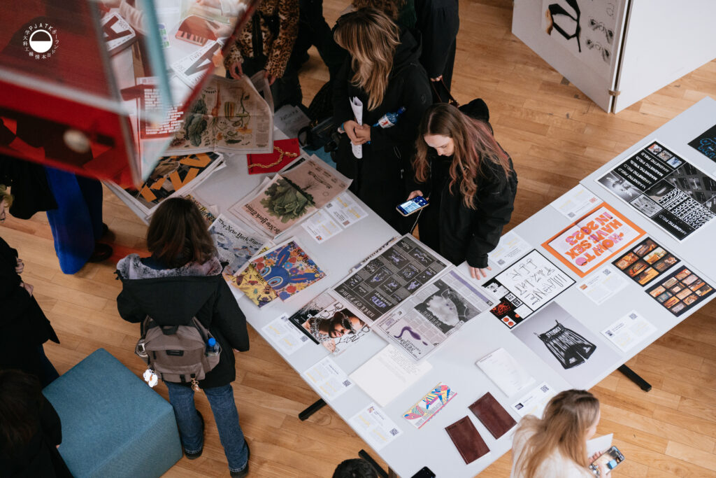 Widok z góry na stół z różnorodnymi projektami graficznymi i osobami je oglądającymi.