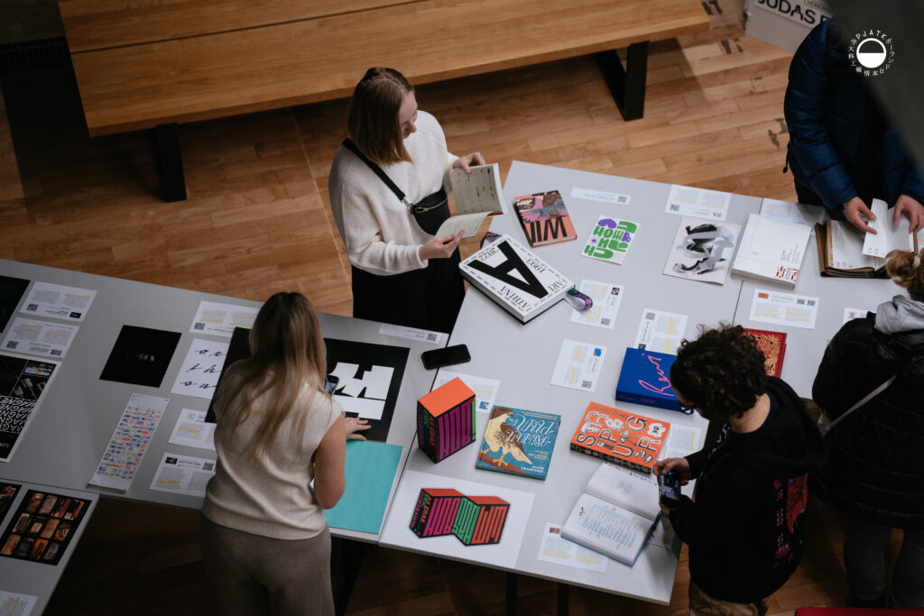 Grupa osób przegląda publikacje i materiały typograficzne podczas wystawy.