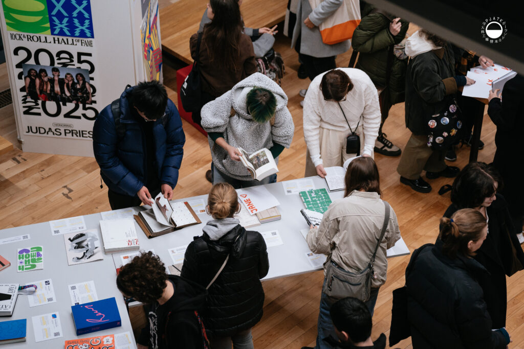 Widok z góry na uczestników oglądających książki i projekty typograficzne na stołach.