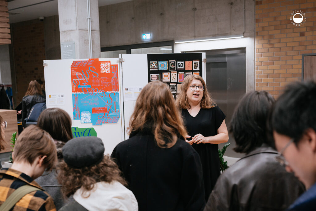 Prowadząca opowiada o projektach typograficznych grupie słuchaczy przy ekspozycji.