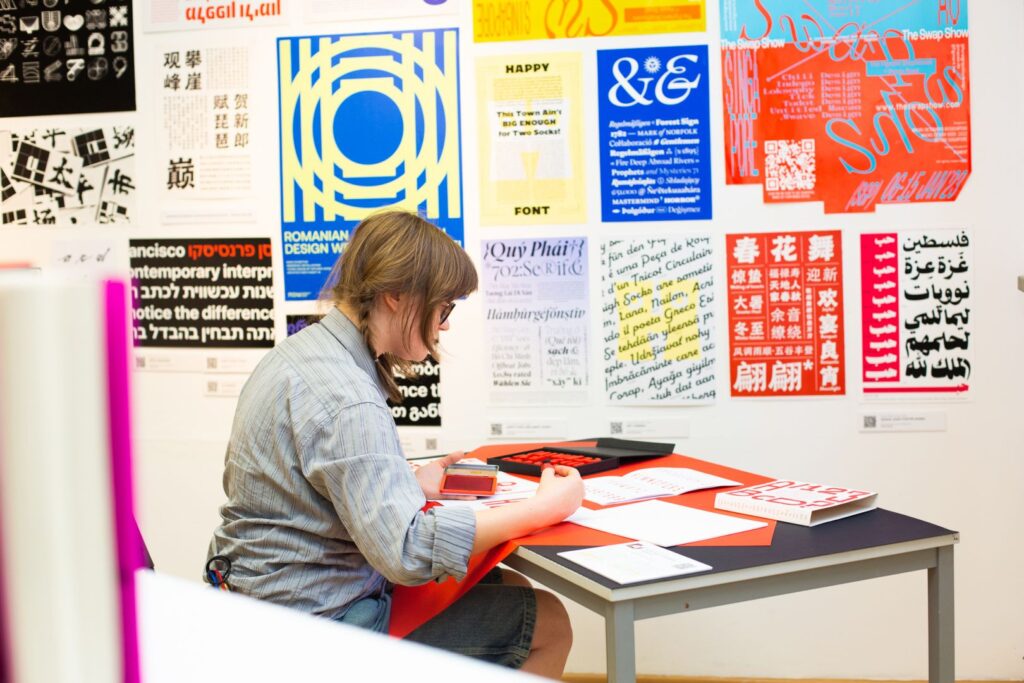 Osoba pracuje przy stole, odbijając typograficzne litery i tworząc własny projekt.