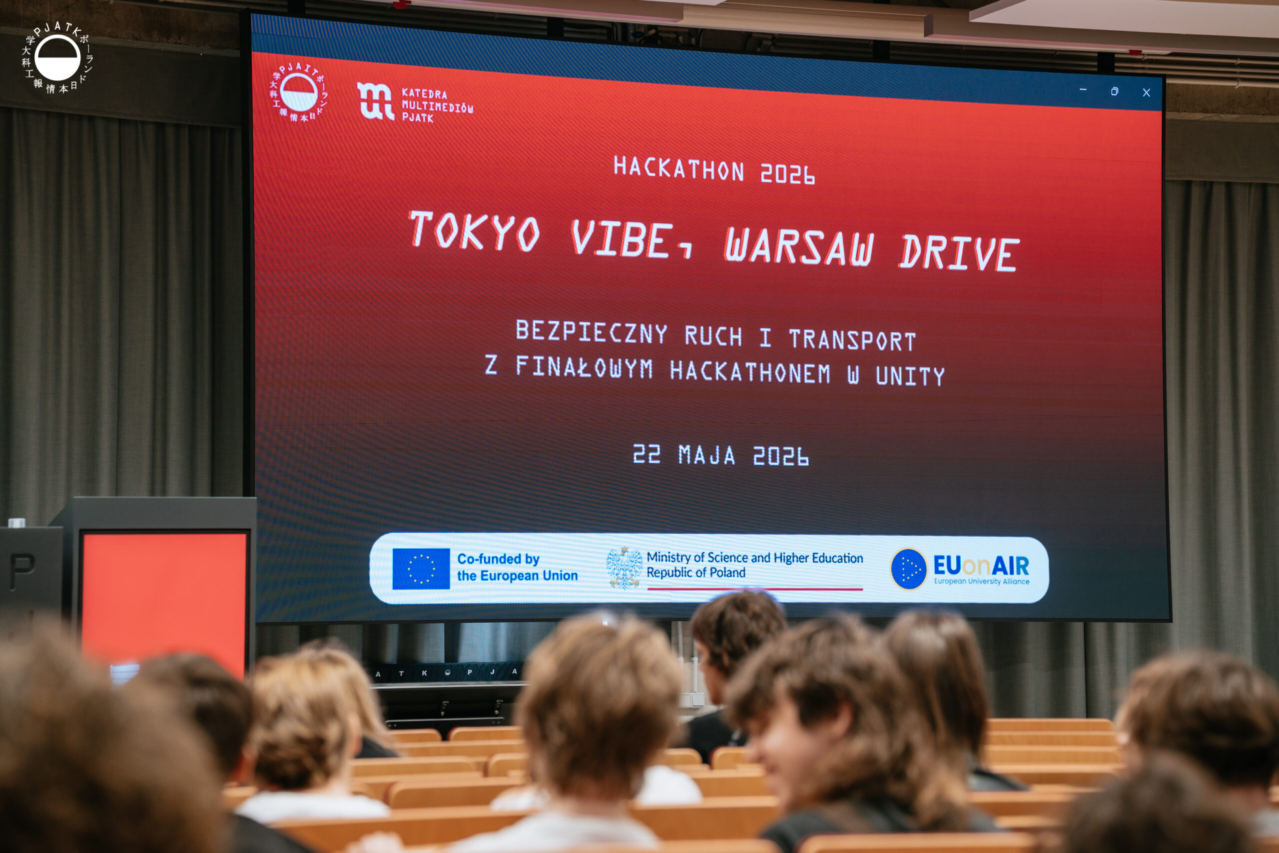 Zdjęcia z wydarzenia „Tokyo vibe, Warsaw drive” w PJATK. Uczestnicy biorą udział w wykładach oraz testują symulator jazdy samochodem przygotowany w ramach projektu Katedry Multimediów. Na fotografiach widać osoby korzystające z kierownicy i ekranów symulatora, widok wirtualnej trasy, prelegentów występujących w auli oraz uczestników spotkania.