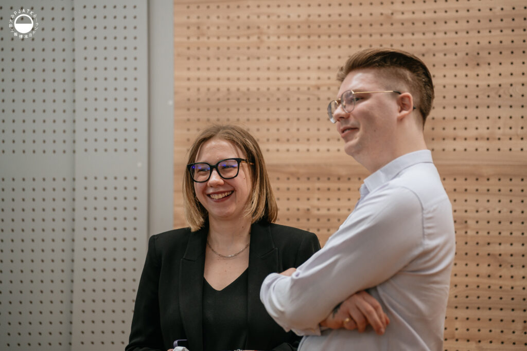 Zdjęcia z wydarzenia „Tokyo vibe, Warsaw drive” w PJATK. Uczestnicy biorą udział w wykładach oraz testują symulator jazdy samochodem przygotowany w ramach projektu Katedry Multimediów. Na fotografiach widać osoby korzystające z kierownicy i ekranów symulatora, widok wirtualnej trasy, prelegentów występujących w auli oraz uczestników spotkania.