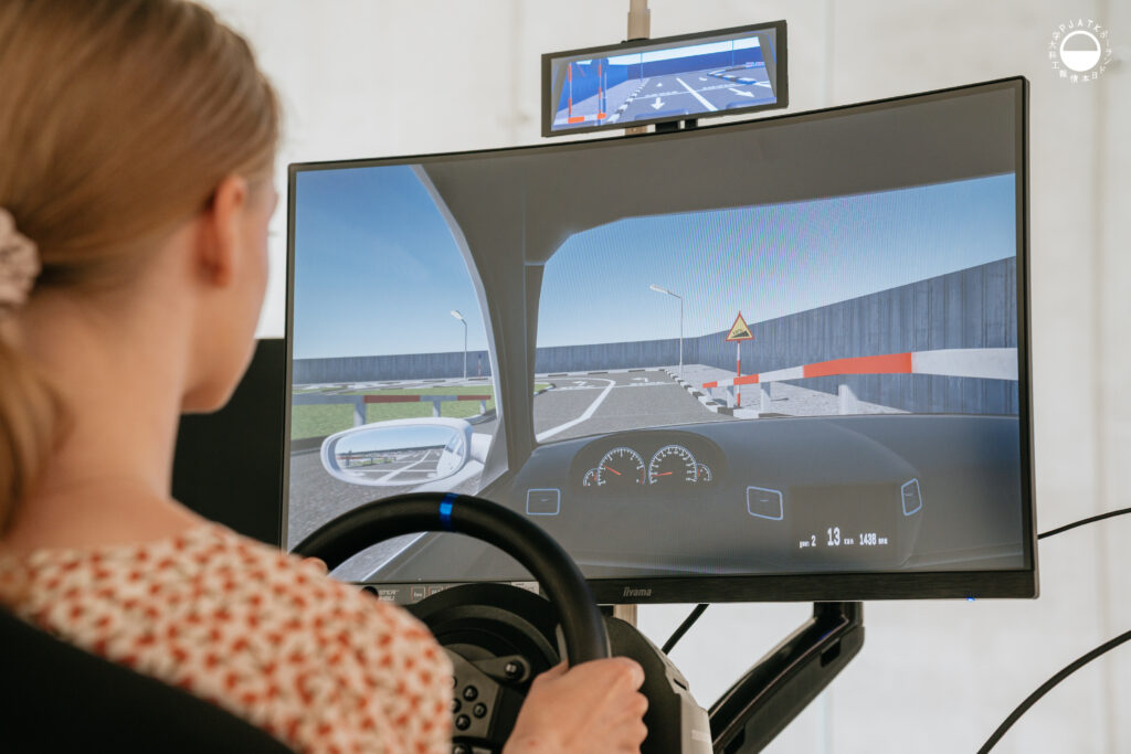 Zdjęcia z wydarzenia „Tokyo vibe, Warsaw drive” w PJATK. Uczestnicy biorą udział w wykładach oraz testują symulator jazdy samochodem przygotowany w ramach projektu Katedry Multimediów. Na fotografiach widać osoby korzystające z kierownicy i ekranów symulatora, widok wirtualnej trasy, prelegentów występujących w auli oraz uczestników spotkania.